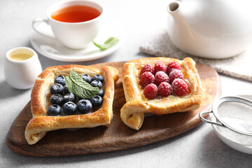Tasty puff pastries with berries and tea on white table, closeup
