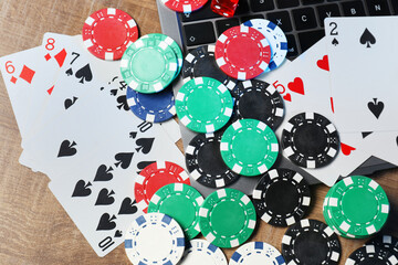 Poker chips, laptop, playing cards and dice on wooden table, flat lay. Online game