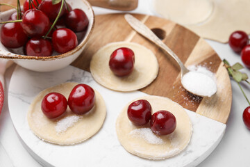 Process of making dumplings (varenyky) with cherries. Raw dough and ingredients on white tiled table
