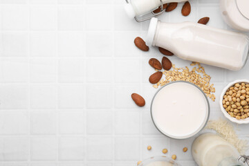 Different types of vegan milk and ingredients on white tiled table, flat lay. Space for text