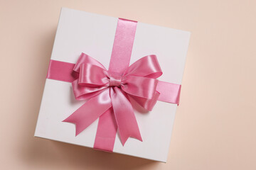 Gift box with bow on beige background, top view