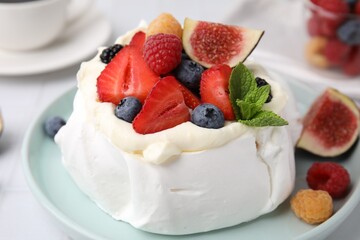 Pavlova cake (meringue dessert) with whipped cream, fresh berries, mint and fig on table, closeup