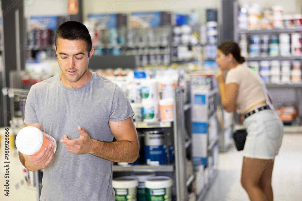 Wall mural Man chooses and buys can of paint at a hardware shop