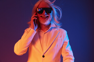 Stylish older man with long white hair and sunglasses engaging in a phone conversation, set against a vibrant colorful background