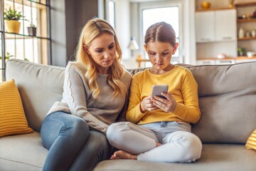 Obraz premium Mom and daughter relaxing on sofa with smartphone
