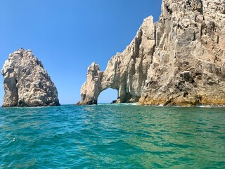 The iconic Arch of Cabo San Lucas rising majestically from the sea on a bright summer day, framed by a stunning blend of deep and vibrant blues from the sky and ocean.