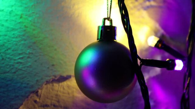 Una toma de cerca de una bola de navidad guindada en varias luces de colores en una pared de color blanco. Decoraci&oacute;n de navidad y fin de a&ntilde;o.