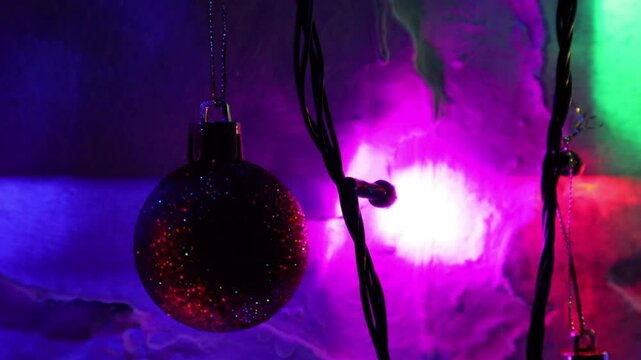 Una toma de cerca de una bola de navidad guindada en varias luces de colores en una pared de color blanco. Decoraci&oacute;n de navidad y fin de a&ntilde;o.