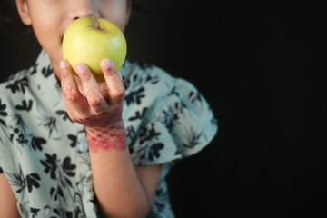 A child joyfully holds a bright green apple, showcasing innocence and cultural henna art