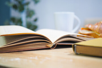 An open book with its pages gently turning rests on a wooden table in the breeze