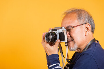Portrait Asian old man wearing glasses look viewfinder vintage SLR camera studio shot isolated yellow background, smiling happy Photographer elderly man gray haired taking a picture of himself