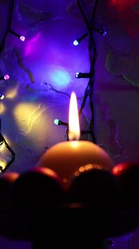 Una toma de cerca de una vela blanca con llama rodeada de bolas y varias luces con bombillos de varios colores en movimiento en la oscuridad