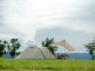 Cream Dome tent pitched on grassy field, mountainside grass field with a few trees in background. Some clouds in sky. Holiday activities