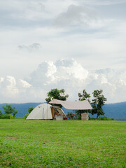 Cream Dome tent pitched on grassy field, mountainside grass field with a few trees in background. Some clouds in sky. Holiday activities