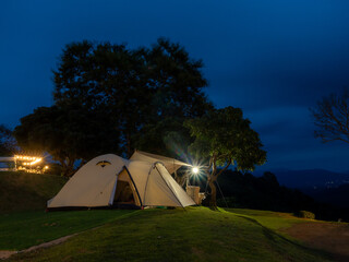 Atmosphere at night very good. Cream Dome tent pitched on grassy field, mountainside grass field with a few trees in background. Some clouds in sky. Holiday activities.