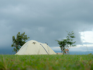 Cream Dome tent pitched on grassy field, mountainside grass field with a few trees in background. Some clouds in sky. Holiday activities