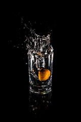 Water splash from inside orange drink glass on black background