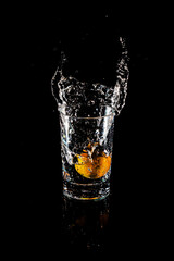 Water splash from inside orange drink glass on black background