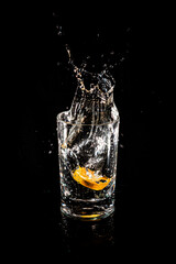 Water splash from inside orange drink glass on black background