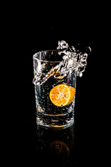 Water splash from inside orange drink glass on black background