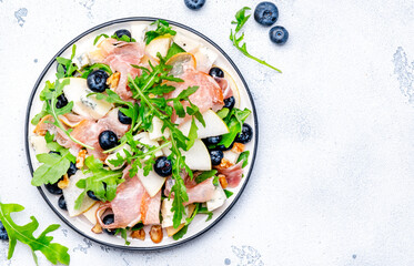Delicious salad with pears, blueberries, blue cheese, smoked ham, arugula and walnuts. White background, top view