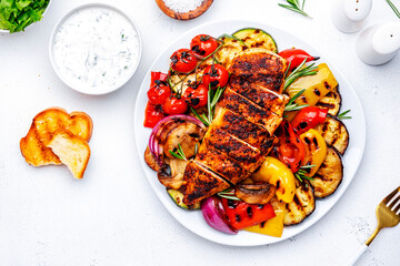 BBQ lunch. Grilled chicken breast and various vegetables on plate, white background, top view