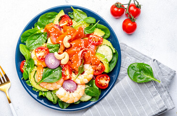 Seafood salad with shrimp, salmon, avocado, spinach, cucumber, tomato, cashew and sesame seeds.. White background, top view