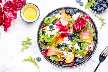 Fresh salad with arugula, radiccio, peaches, smoked ham, ricotta cheese and blueberries. White...