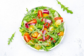 Vegan vegetable salad with tomatoes, cucumber, onion, lettuce and arugula. White background, top view