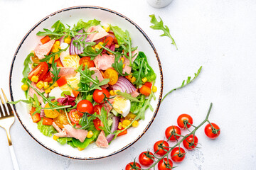 Tasty tuna vegetable salad with tomatoes, onion, corn, eggs, paprika, lettuce and arugula. White  background, top view