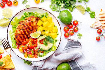 Mexican salad bowl with grilled chicken and mango, tomato, cilantro, onion and lettuce, white background, top view