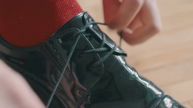 Gentleman Fastening Glossy Dress Shoe. Luxury Footwear Close-up. Hands Securing Patent Leather Loafers. Crimson Sock on Hardwood. Formal Attire Preparation. Sophisticated Male Grooming Detail