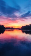 Obraz premium The image showcases a stunning sunset over a calm lake. The sky is painted with vibrant hues of pink, purple, orange, and blue, creating an ethereal atmosphere. The reflections of the colorful sky on 