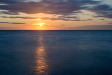 sunset over calm ocean water as the evening light reflects over the sea