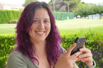 A woman with purple hair is holding a cell phone and smiling