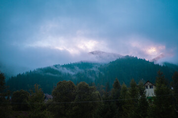Naklejka premium A tranquil morning in the mountains with mist rising above the trees and a faint glow of dawn illuminating the clouds