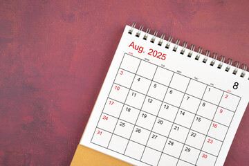 August 2025 desk calendar on red background.