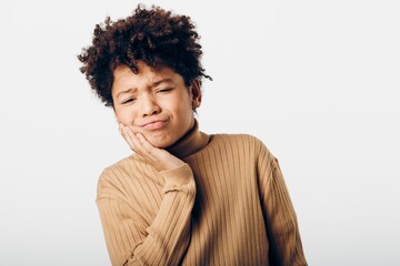 Young african american boy clutching his cheek in pain, displaying signs of a toothache against a...