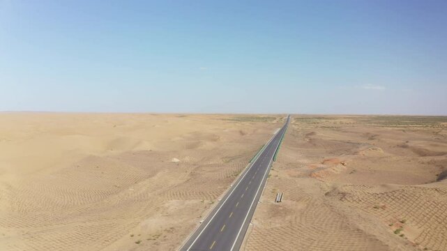 Car driving on the highway in the Gobi Desert, Inner Mongolia. Panning drone footage showing road infrastructure in the desert. A well-maintained highway surrounded by sand dunes in Bayannur, China.