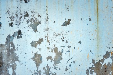 The wall is covered in peeling paint and has a rough texture. The blue color of the wall is faded and has a worn appearance. The wall has a lot of cracks and holes, giving it a sense of decay