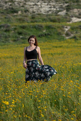 Young woman wearing long green dress walking in the blooming spring field outdoors. Female person active outdoor