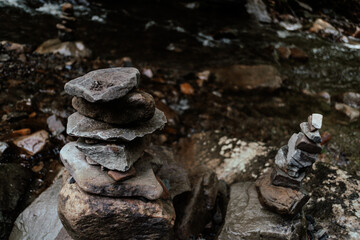 Stacked stones create a serene balance beside a gentle stream in a tranquil forest setting during the day