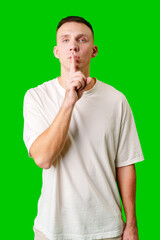 Young Man Gesturing for Silence With a Finger to His Lips Against a Bright Green Background