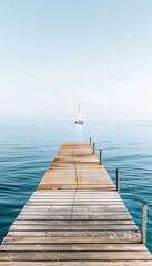 Fototapeta premium Serene wooden dock extending into tranquil blue waters with sailboat under clear skies