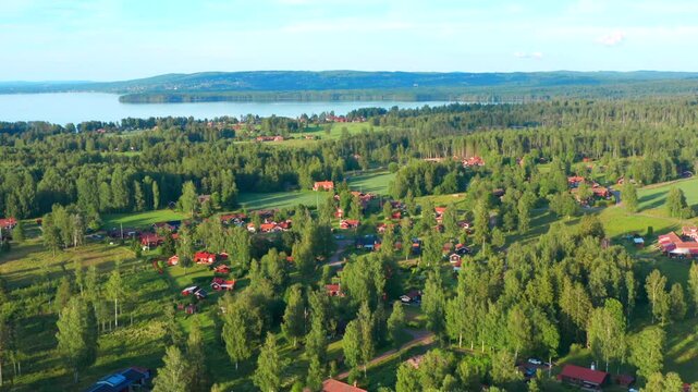 Summer houses in Sweden hidden in the forest between trees. Green beautiful surroundings with lake in background. Summer evening aerial drone shot of swedish finest nature
