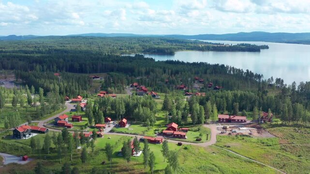 Modern newly built red swedish summer houses by lake and forest. Sweden in summer time country site vacation rental homes. Aerial flight over community in Dalarna Siljan