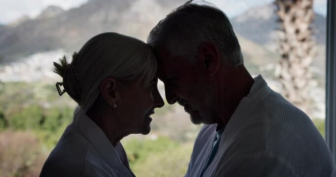 Happy, senior couple and holiday with hug by window for marriage, bonding and vacation on anniversary. Man, woman and forehead touch with love in house for getaway, romance and commitment connection