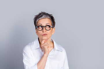 Portrait of elegant aged lady office worker look empty space ponder wear shirt isolated on grey...