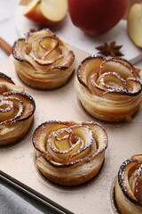 Freshly baked apple roses in cupcake pan on table, closeup. Puff pastry