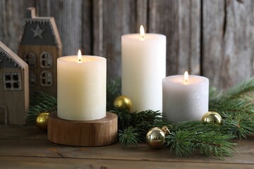 Burning candles, baubles, fir branches and other Christmas decor on wooden table